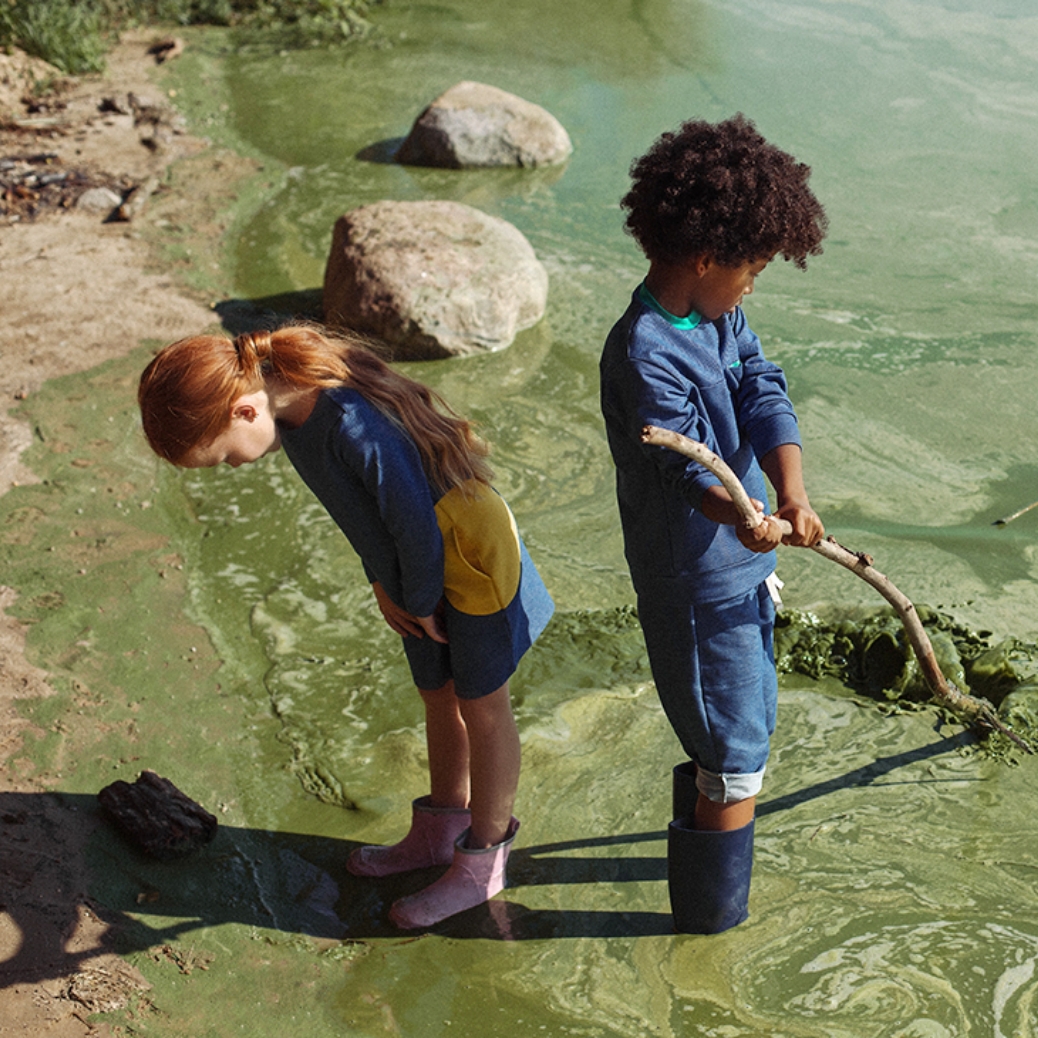 two kids playing in a river wearing boots.